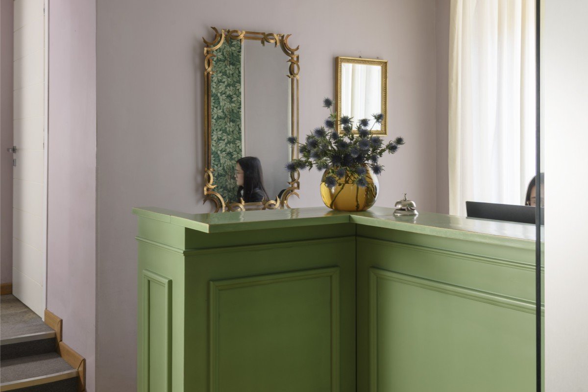 Reception desk in Rome Monti district with green counter, vintage golden mirror, flower vase and natural light - Salotto Monti, BZAR hotels in Rome
