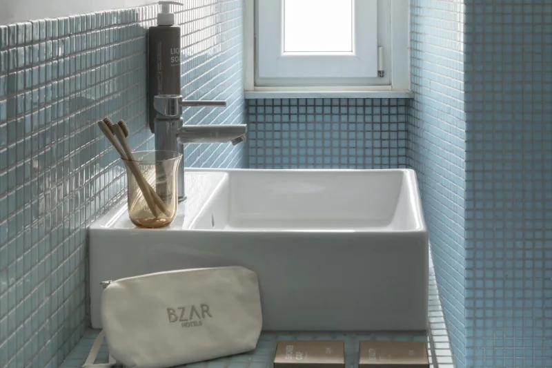 Bagno con vasca nel rione Monti Roma con piastrelle azzurre, lavabo moderno e luce naturale da finestra - Salotto Monti, BZAR hotels a Roma