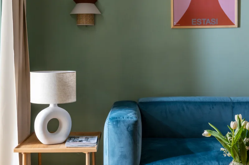 Dettaglio soggiorno nel quartiere Monti Roma con divano blu, lampada design e parete verde decorativa - Salotto Monti, BZAR hotels a Roma