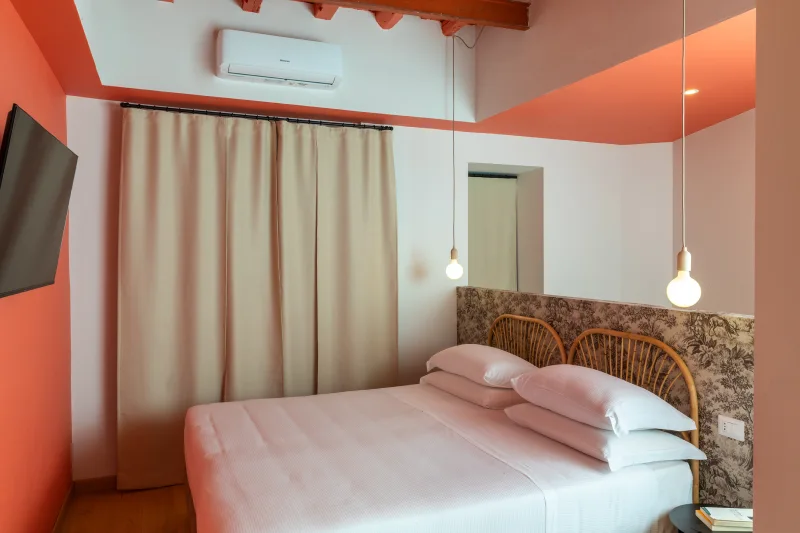Camera appartamento nel rione Monti Roma con pareti rosse, travi a vista, letto matrimoniale e luci sospese - Salotto Monti, BZAR hotels a Roma