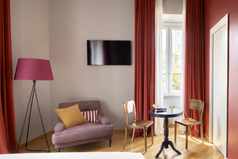 Junior Suite in Rome Monti area with lounge corner, lilac sofa, bistro table, wall TV and red curtains - Salotto Monti, BZAR hotels in Rome