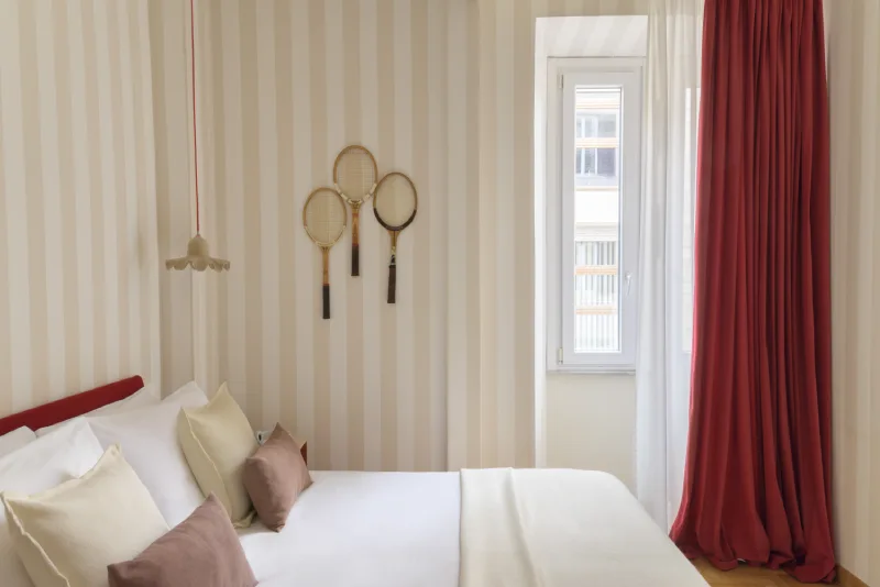 Bright double room in Rome Monti district with beige pillows, striped walls, decorative rackets and red curtains - Salotto Monti, BZAR hotels in Rome