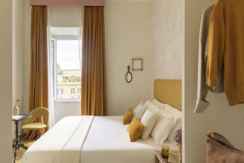 Double room in Rome Monti district with white bed, ochre cushions, elegant curtains and view of historic buildings - Salotto Monti, BZAR hotels in Rome