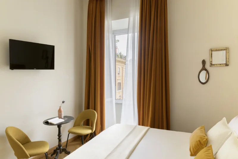 Room corner in Rome Monti area with small table, design chairs, wall TV and bright window with ochre curtains - Salotto Monti, BZAR hotels in Rome