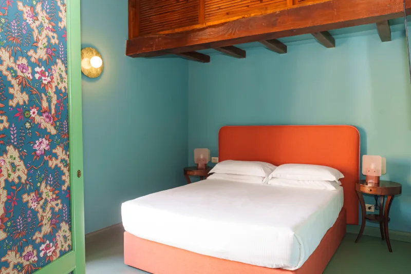 Colorful room in Rome Monti district with turquoise walls, bed with orange headboard and wooden mezzanine - Salotto Monti, BZAR hotels in Rome
