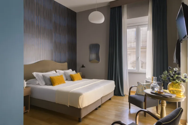 Bright superior room in Rome Monti district with king bed, yellow cushions, window with curtains and table with tray - Salotto Monti, BZAR hotels in Rome