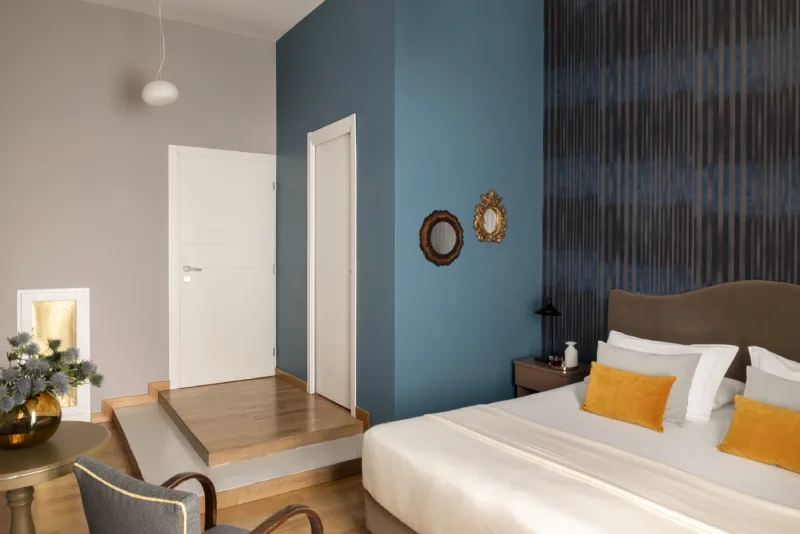 Superior room in Rome Monti area with blue feature wall, bed with yellow cushions, decorative details and wooden floor - Salotto Monti, BZAR hotels in Rome
