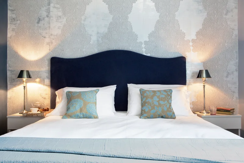 Bed detail in a superior room in Rome Monti district with blue headboard, elegant wallpaper and bedside lamps - Salotto Monti, BZAR hotels in Rome