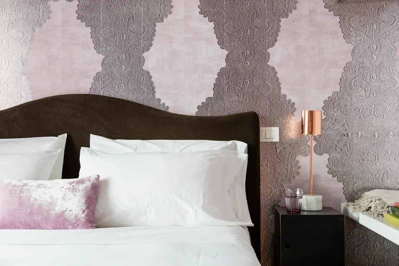 Close-up room detail in Rome Monti area with dark headboard, lilac patterned wallpaper, copper lamp and minimal bedside table - Salotto Monti, BZAR hotels in Rome