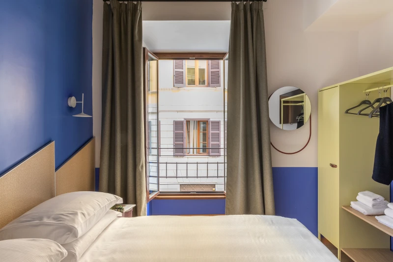 Prima camera matrimoniale nel quartiere Monti Roma con parete blu, finestra su edifici storici e guardaroba aperto - Salotto Monti, BZAR hotels a Roma